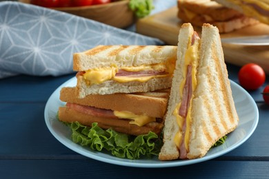 Photo of Tasty sandwiches with ham, melted cheese and lettuce on blue wooden table, closeup