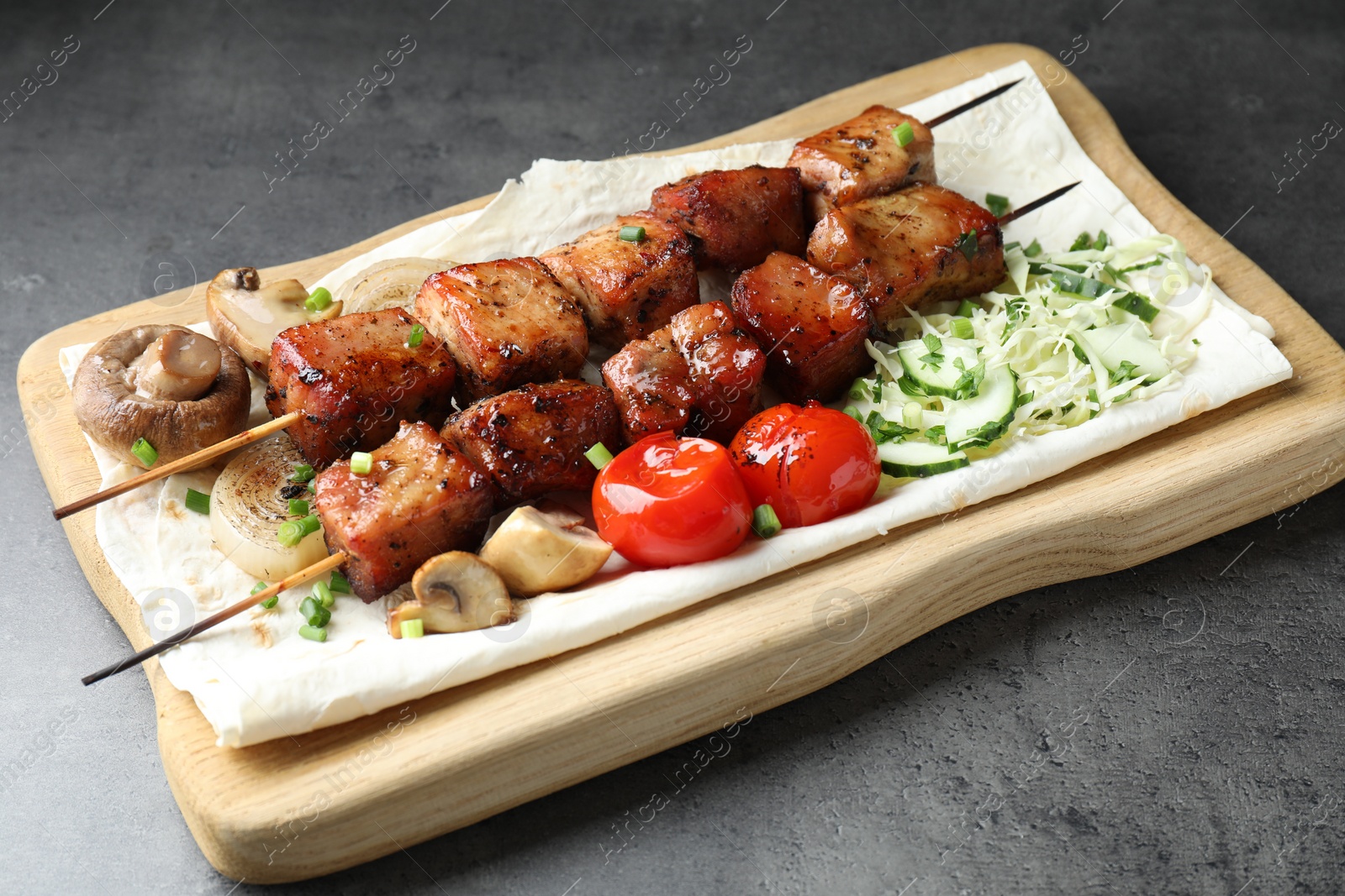 Photo of Delicious shish kebabs with vegetables and lavash on grey table