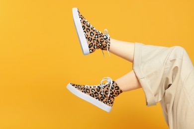 Photo of Woman posing in classic old school sneakers with leopard print on orange background, closeup. Space for text