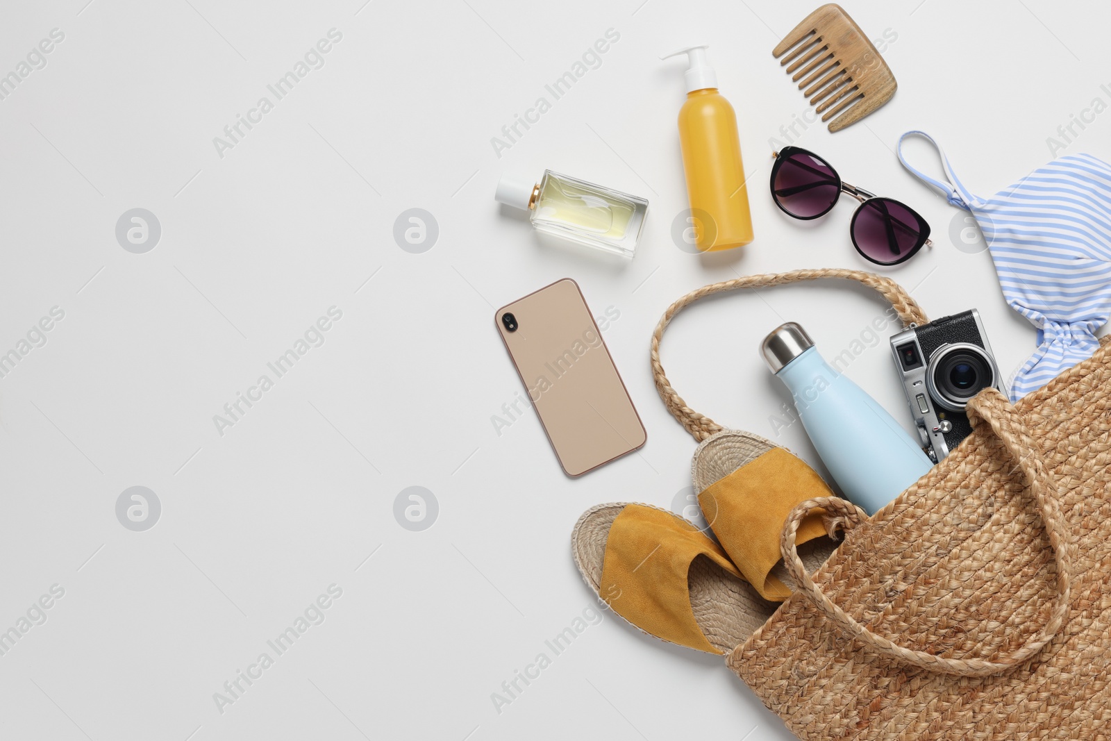 Photo of Wicker bag, smartphone and beach accessories on white background, flat lay. Space for text