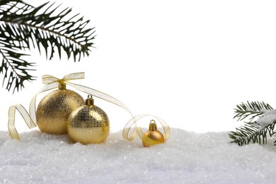 Photo of Beautiful golden Christmas balls with bow and fir tree branches on snow against white background