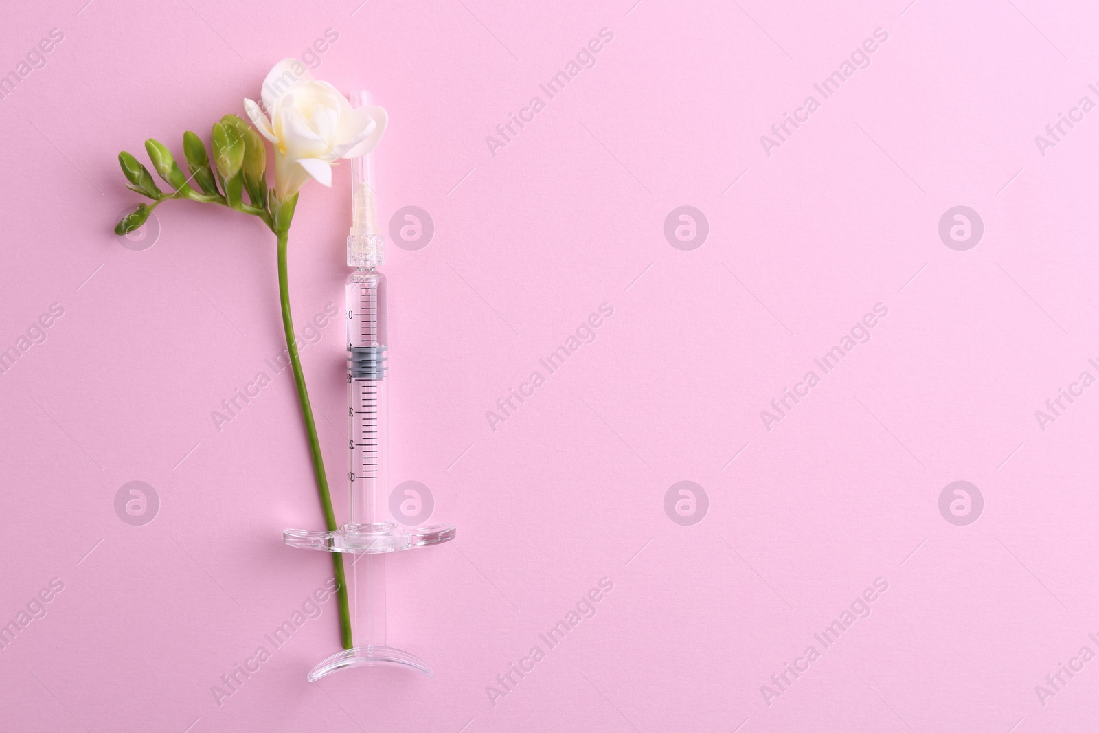 Photo of Cosmetology. Medical syringe and freesia flower on pink background, top view. Space for text