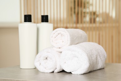 Photo of Soft folded terry towels and cosmetic bottles on light gray table indoors