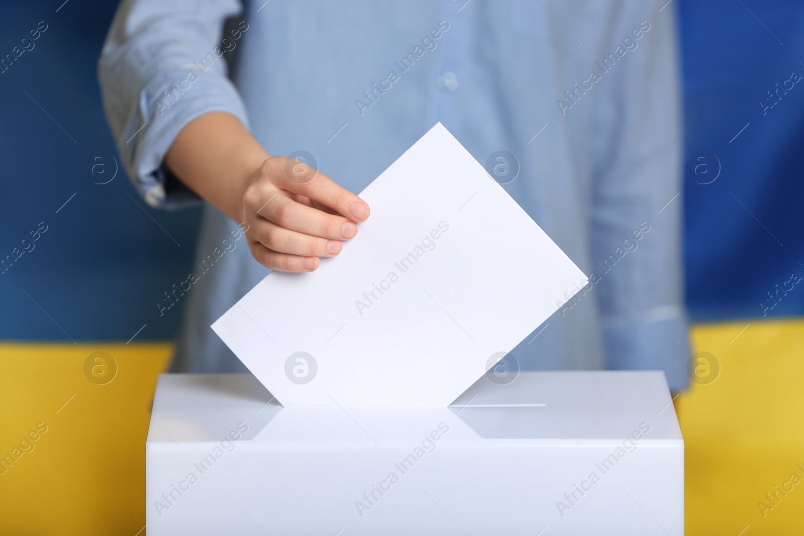 Photo of Woman putting voting paper into ballot box against Ukrainian flag, closeup