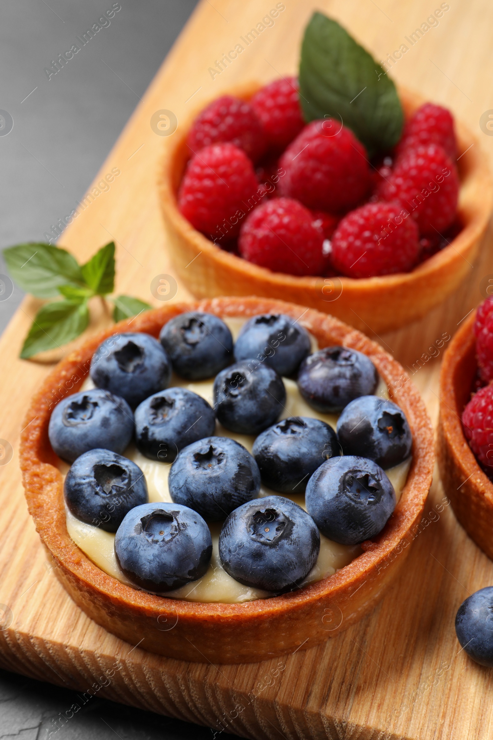 Photo of Tartlets with different fresh berries on wooden board, closeup. Delicious dessert