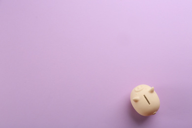 Beige piggy bank on violet background, top view. Space for text
