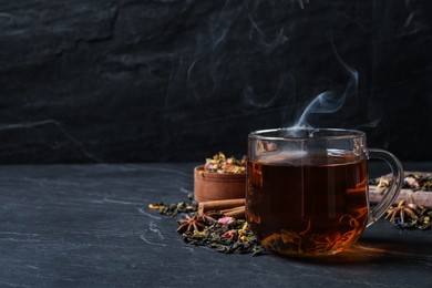 Glass cup of freshly brewed tea and dry leaves on black table. Space for text