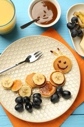 Photo of Creative serving for kids. Plate with cute caterpillar made of pancakes, grapes and banana on light blue wooden table, flat lay