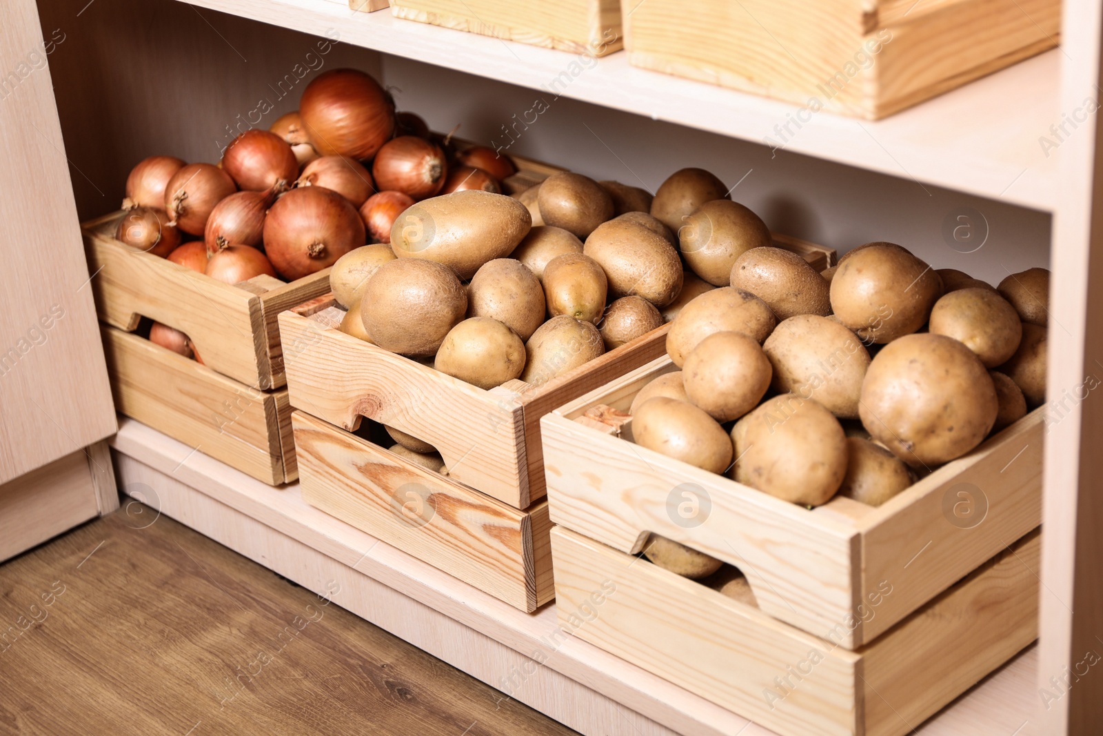Photo of Crates with potatoes and onions on shelf. Orderly storage