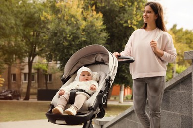 Photo of Young mother walking with her adorable baby in stroller outdoors