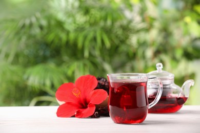 Delicious hibiscus tea and flowers on white wooden table outdoors, space for text