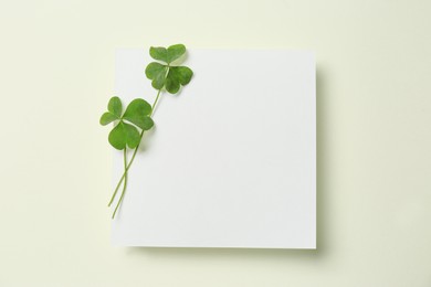 Photo of Green clover leaves and blank card on light background, top view. Space for text