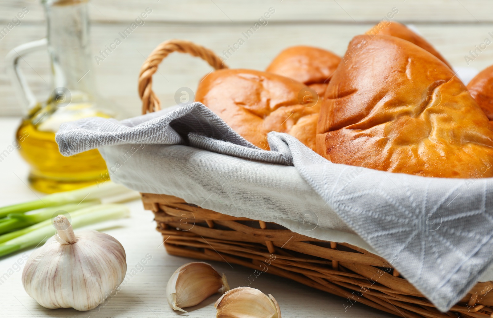 Photo of Wicker basket with delicious baked patties and garlic on white wooden table