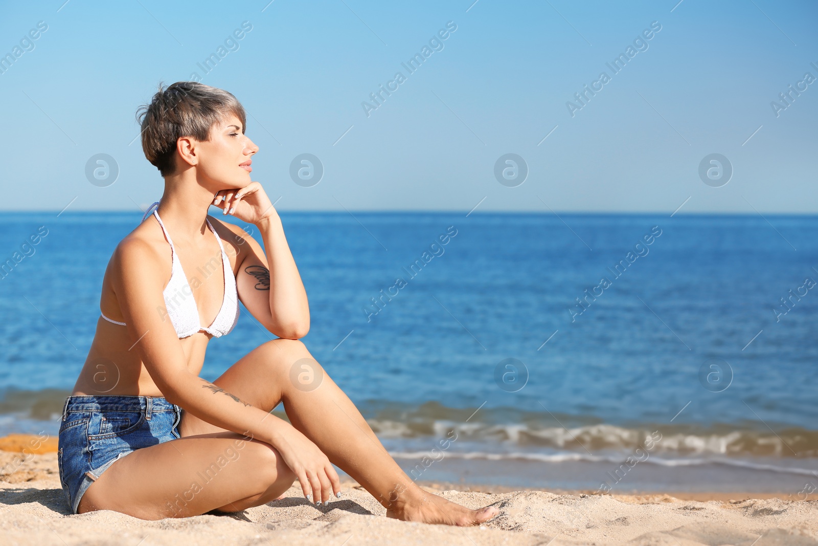 Photo of Young woman sitting on beach. Space for text