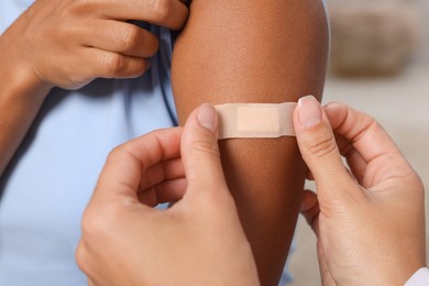 Photo of Doctor putting adhesive bandage on young woman's arm after vaccination indoors, closeup