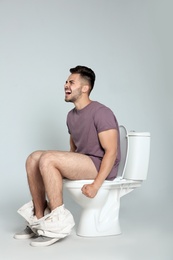 Photo of Young man suffering from diarrhea on toilet bowl against gray background
