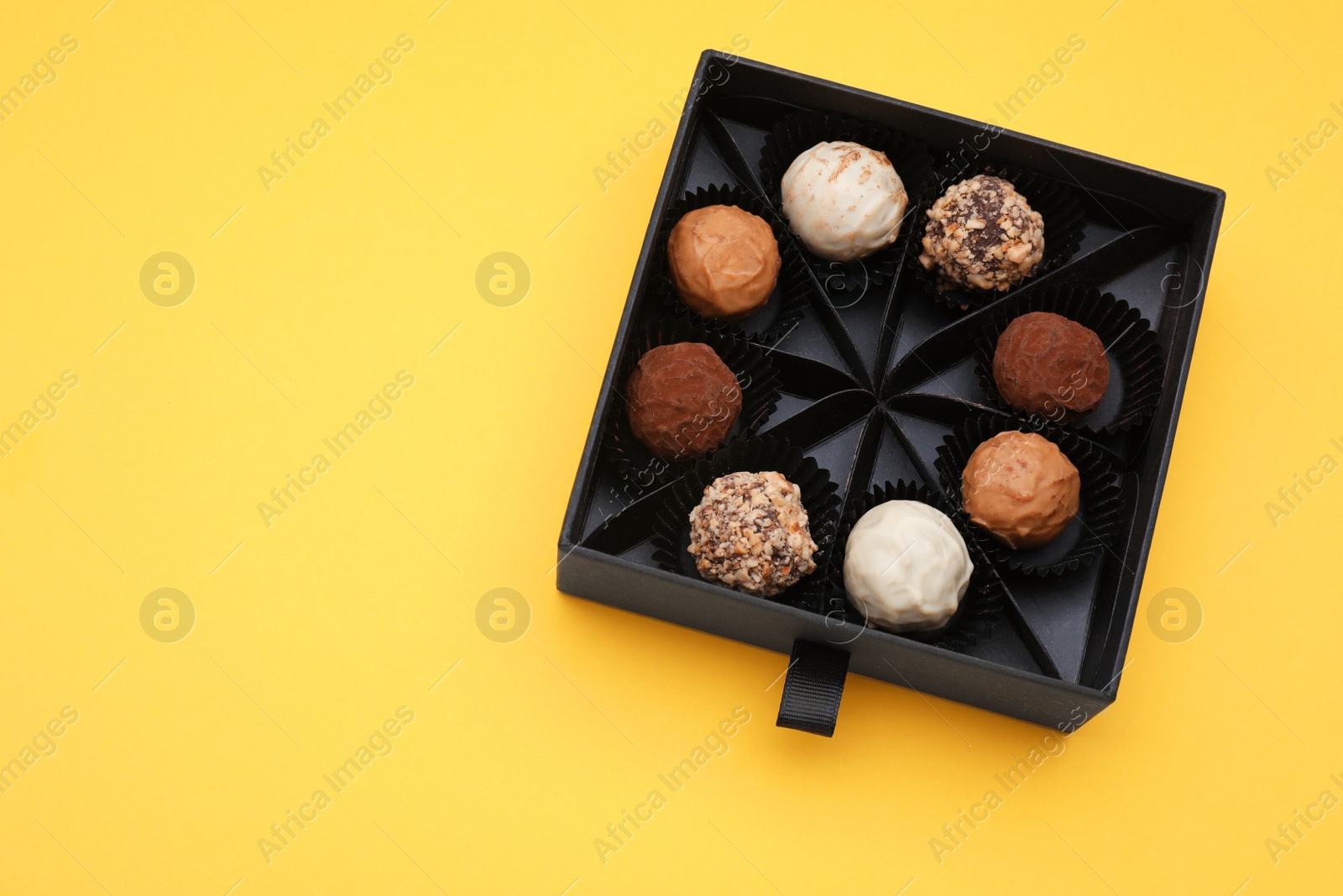 Photo of Box of tasty chocolate candies on yellow background, top view. Space for text