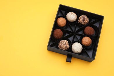 Photo of Box of tasty chocolate candies on yellow background, top view. Space for text