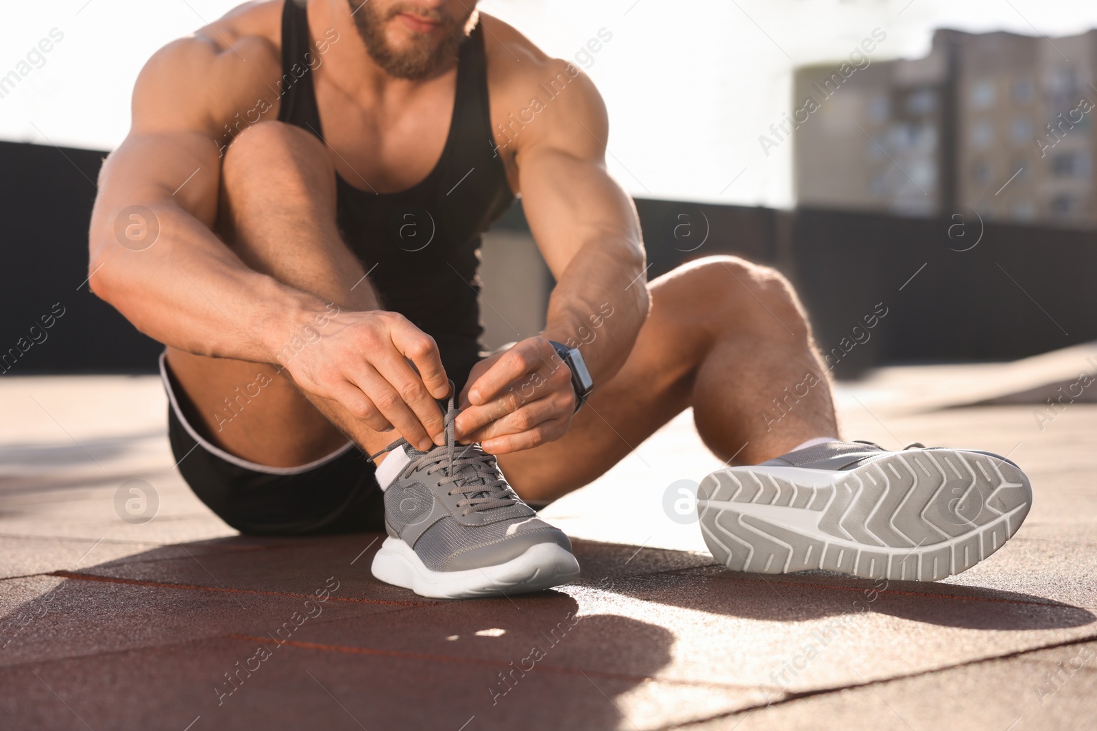 Photo of Man tying shoelaces before running outdoors on sunny day, closeup