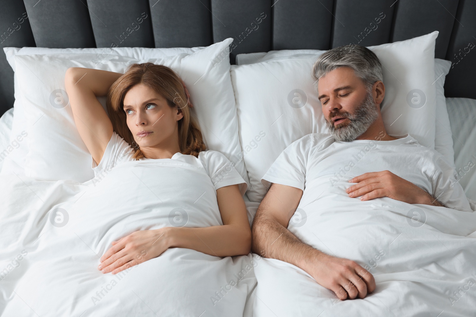 Photo of Irritated woman lying near her snoring husband in bed at home