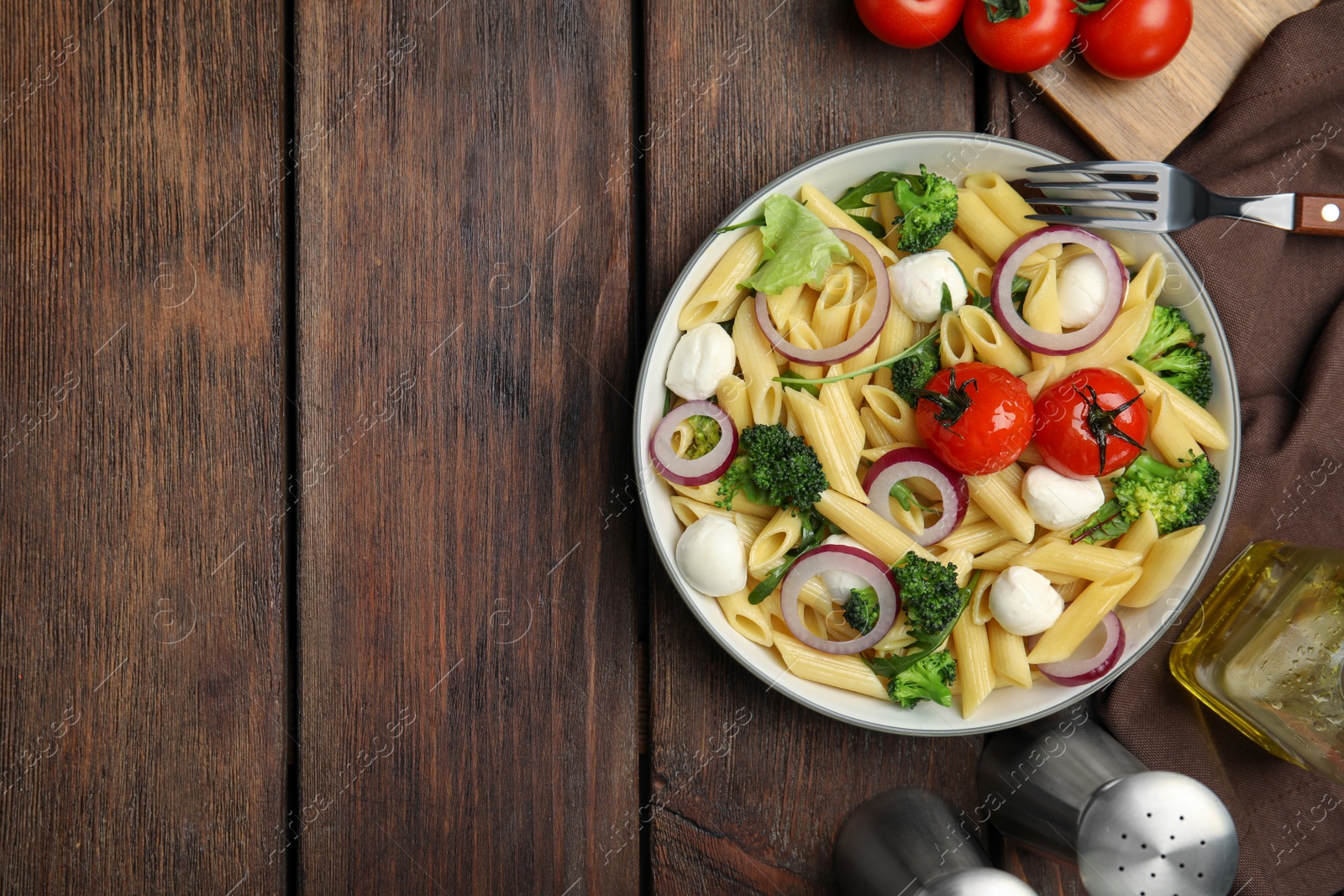 Photo of Bowl of delicious pasta with tomatoes, onion and broccoli on wooden table, flat lay. Space for text