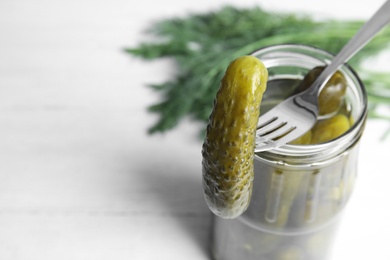 Photo of Fork with marinated cucumber over jar on white wooden table, closeup with space for text