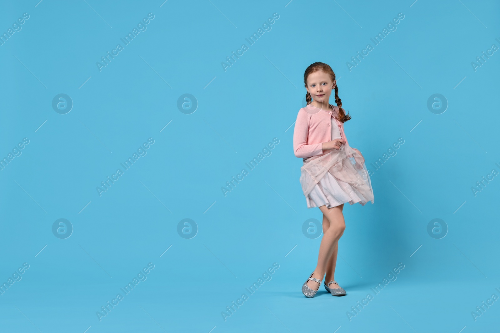 Photo of Cute little girl dancing on light blue background, space for text