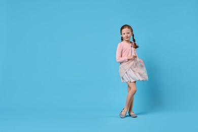 Photo of Cute little girl dancing on light blue background, space for text