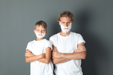 Father and son with shaving foam on faces against color background