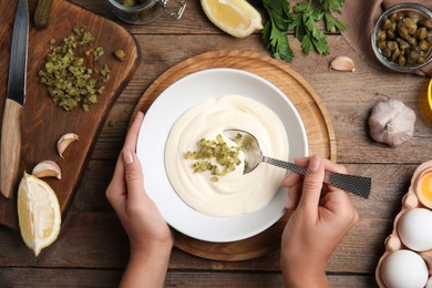 Photo of Woman making delicious tartar sauce at wooden table, top view