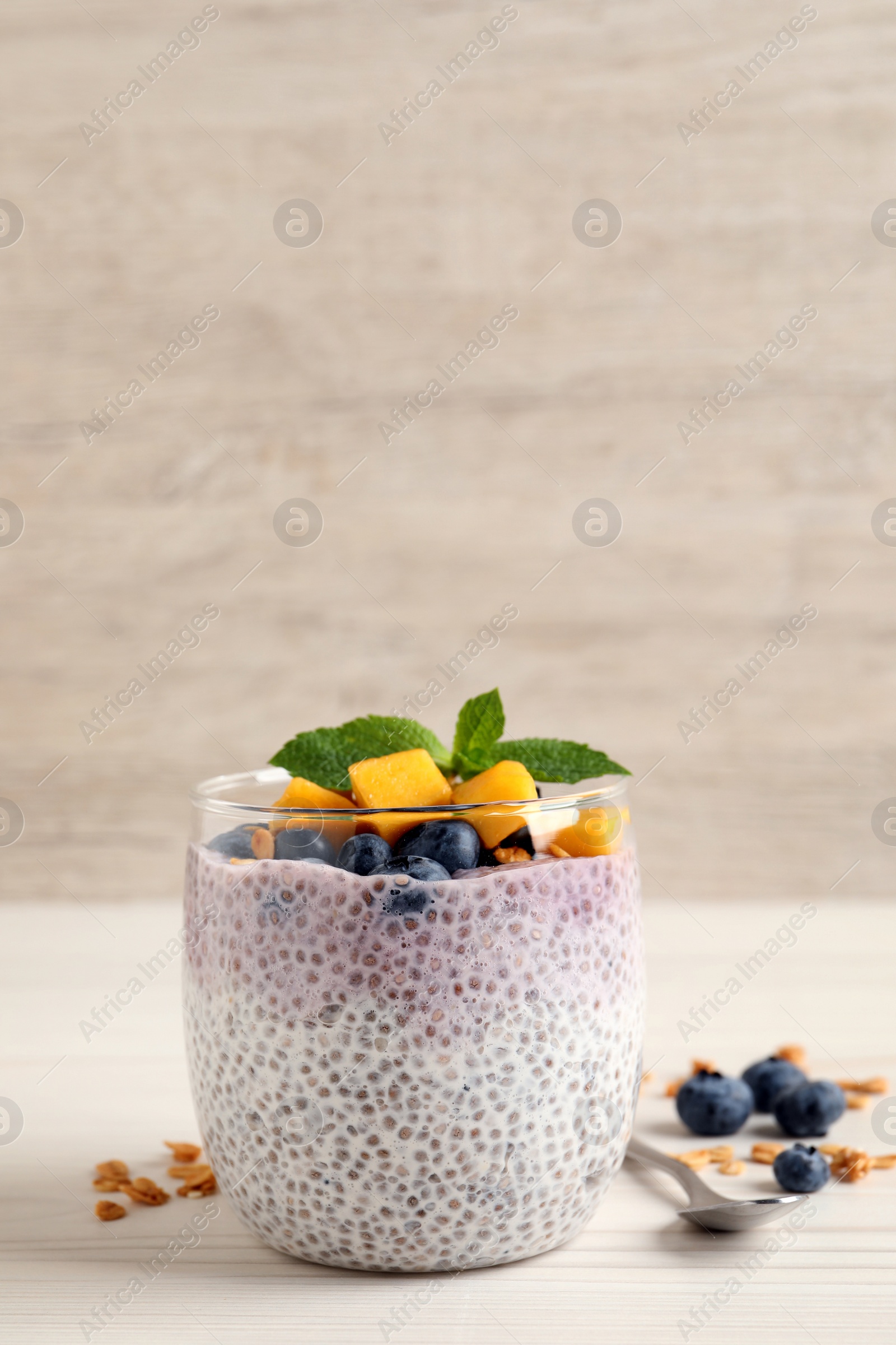 Photo of Delicious chia pudding with blueberries, mango and mint on white wooden table, space for text