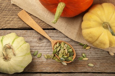 Photo of Spoon with peeled seeds and fresh pumpkins on wooden table, flat lay