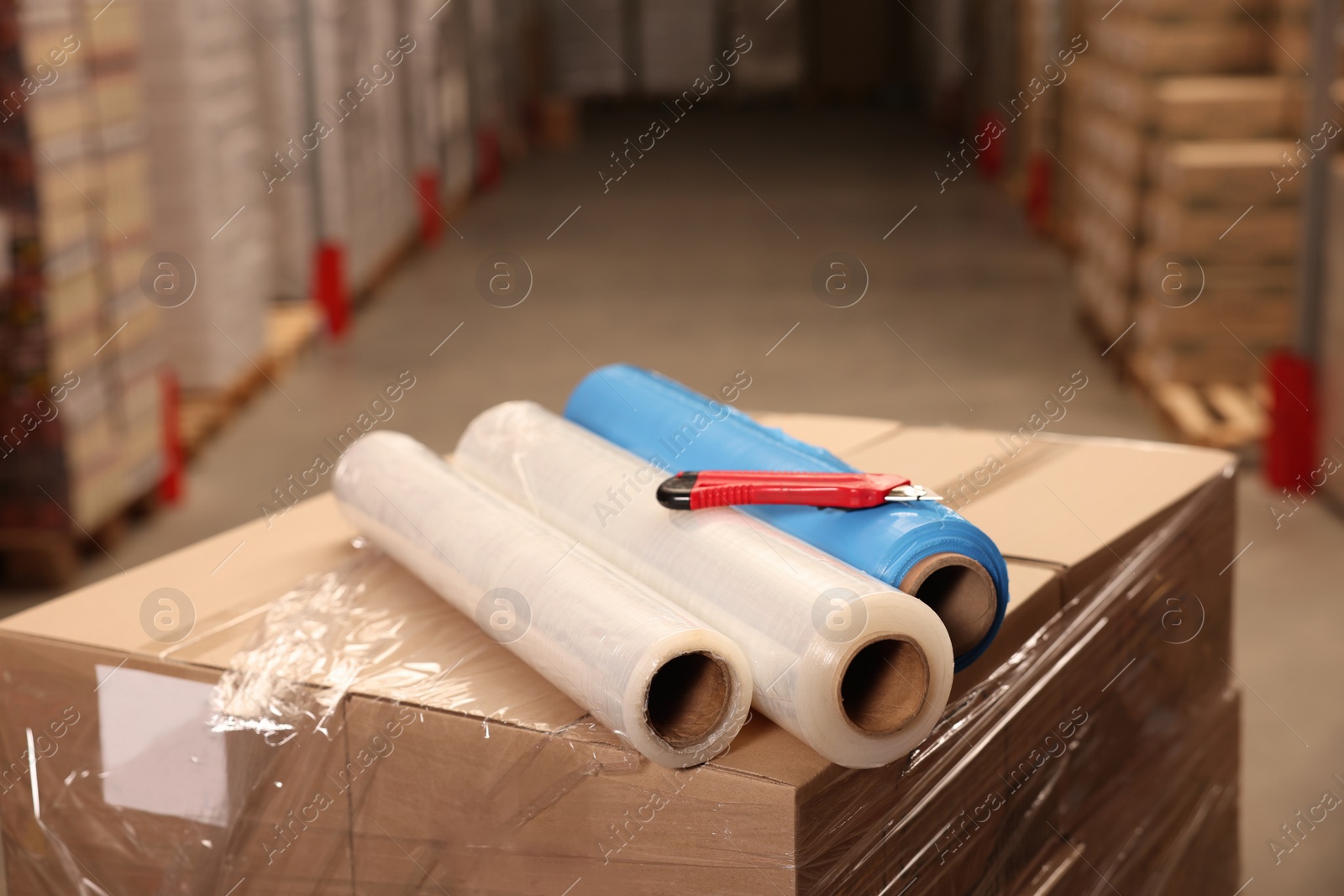 Photo of Rolls of different stretch wraps and utility knife on boxes in warehouse