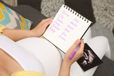 Photo of Pregnant woman with baby names list sitting on sofa, closeup