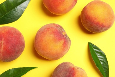 Delicious juicy peaches and green leaves on yellow background, flat lay