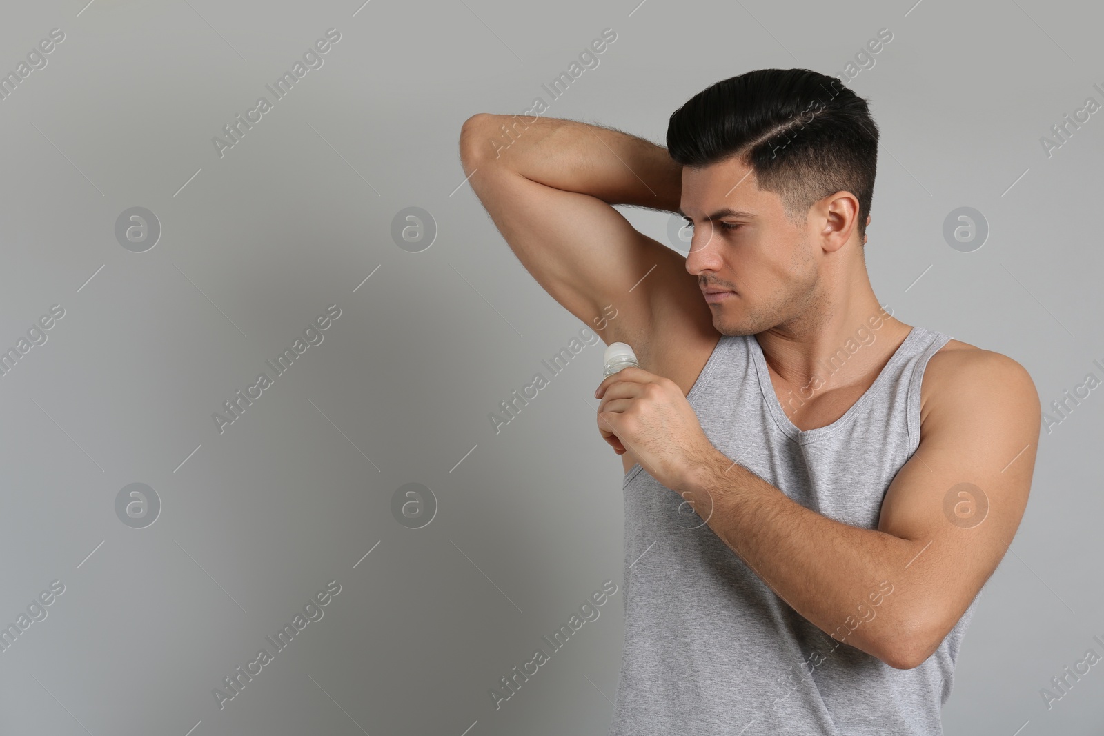 Photo of Handsome man applying deodorant to armpit on grey background, space for text