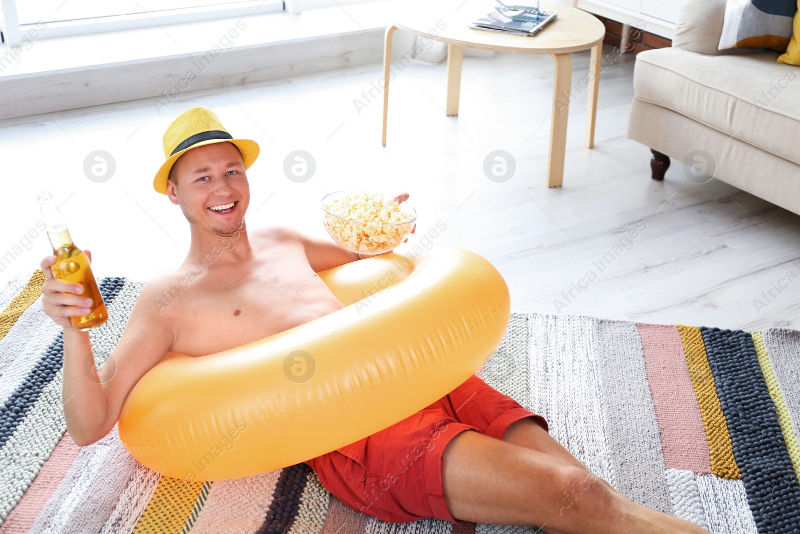 Photo of Shirtless man with inflatable ring, drink and popcorn on floor at home
