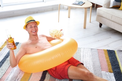 Shirtless man with inflatable ring, drink and popcorn on floor at home