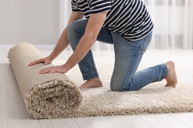 Photo of Man unrolling carpet on floor in room, closeup