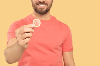 Photo of Man holding condom on beige background, closeup and space for text. Safe sex