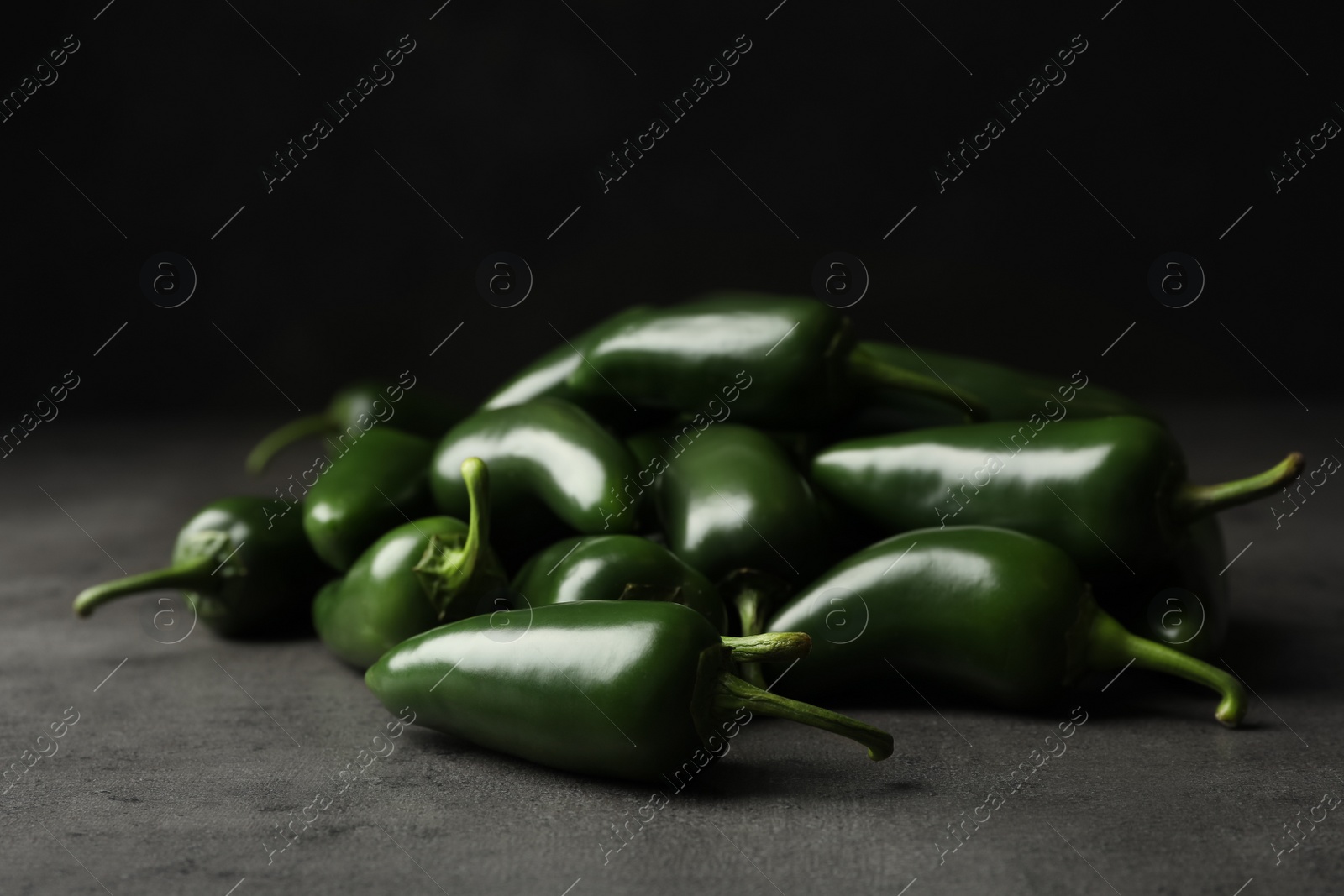 Photo of Pile of green hot chili peppers on grey table, closeup