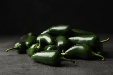 Photo of Pile of green hot chili peppers on grey table, closeup