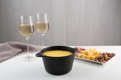 Photo of Fondue with tasty melted cheese, different products and aromatic wine in glasses on white table