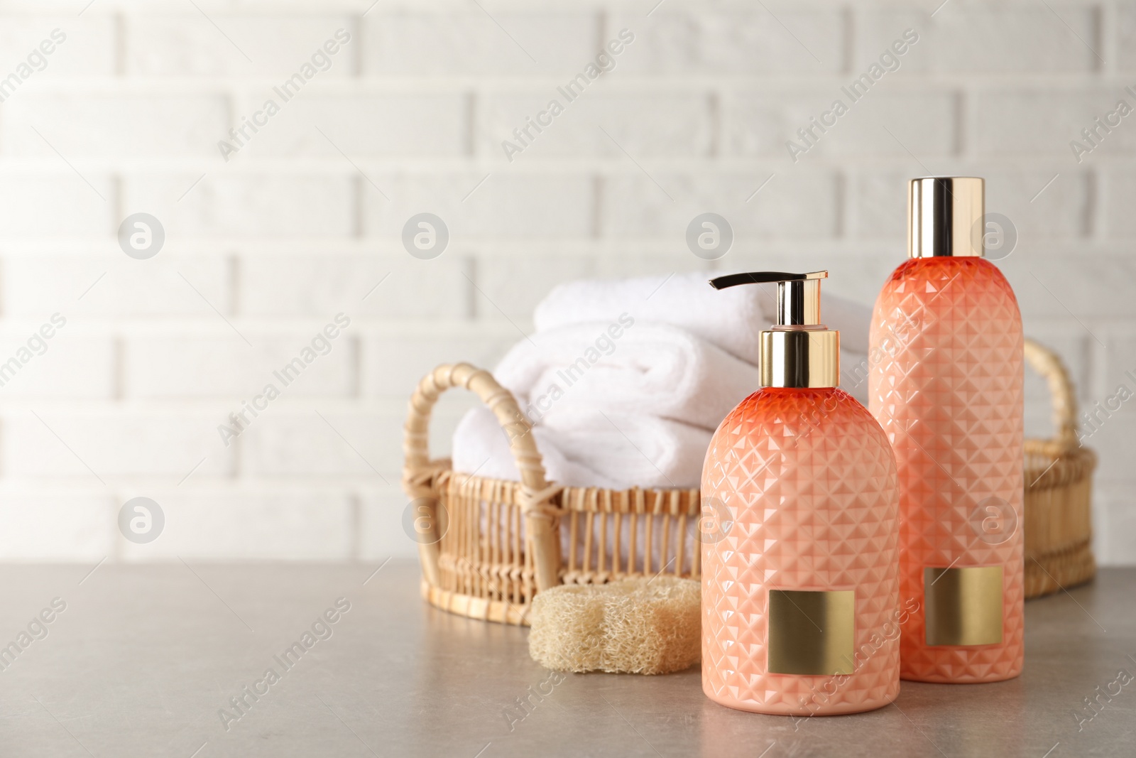 Photo of Stylish dispenser with liquid soap and other bathroom amenities on grey table near white brick wall, space for text