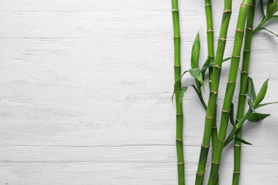 Photo of Green bamboo stems on white wooden background, top view. Space for text