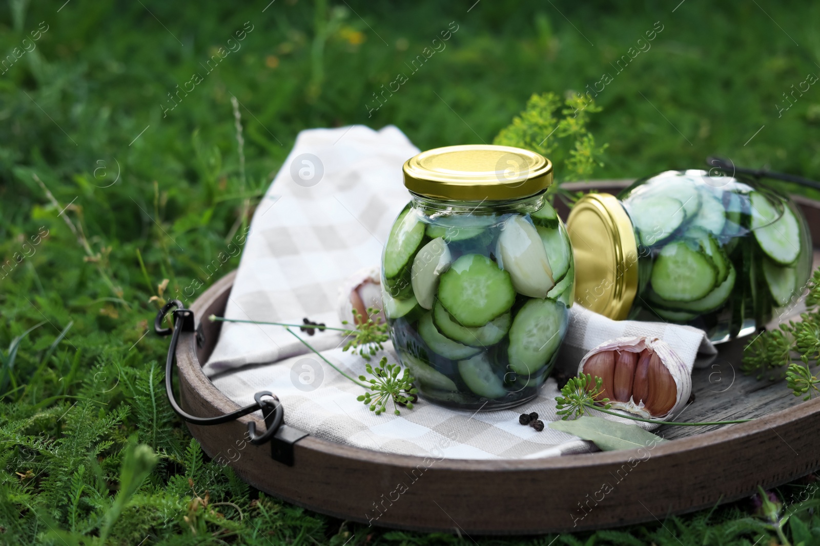 Photo of Jar of delicious pickled cucumbers on wooden tray outdoors. Space for text
