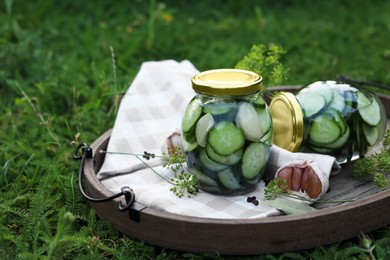 Photo of Jar of delicious pickled cucumbers on wooden tray outdoors. Space for text