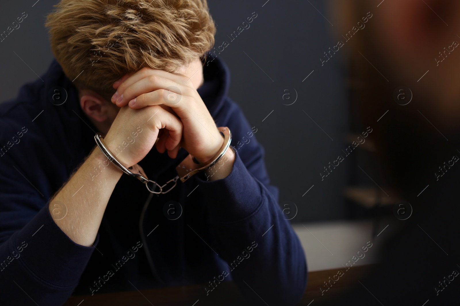 Photo of Man detained in handcuffs at desk indoors. Criminal law