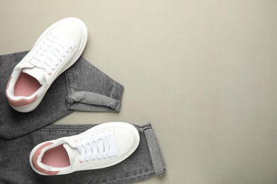 Photo of Stylish white sneakers and jeans on grey background, flat lay. Space for text