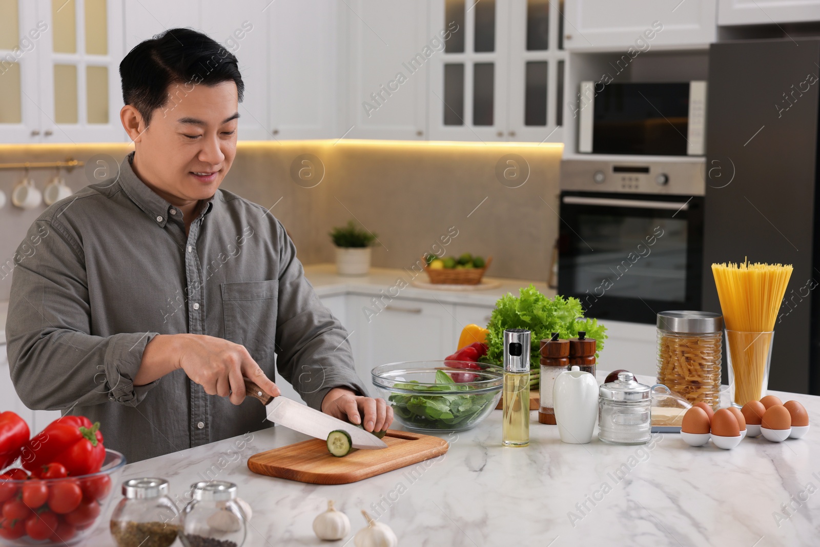 Photo of Cooking process. Man cutting fresh cucumber at countertop in kitchen